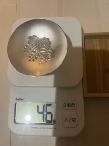 銀色の模様入りの小皿がデジタルスケールに載せられ、スケールは46グラムを表示している。